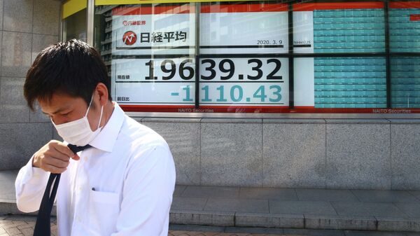 Мужчина в защитной маске на фоне табло с котировками ценных бумаг в Токио, Япония