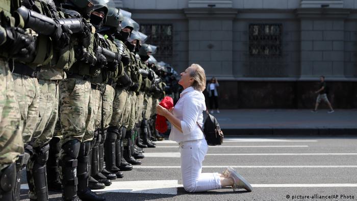 Woman kneels before a police linke in Minsk 